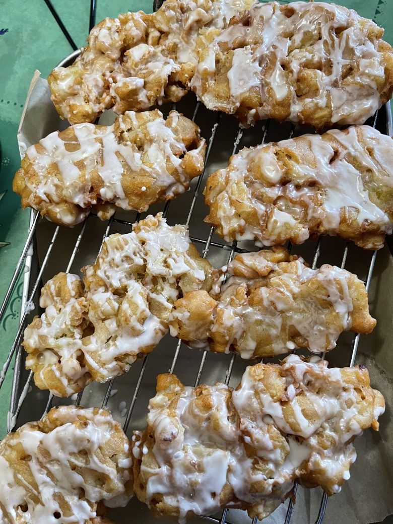 Freshly glazed apple fritters cooling on a rack