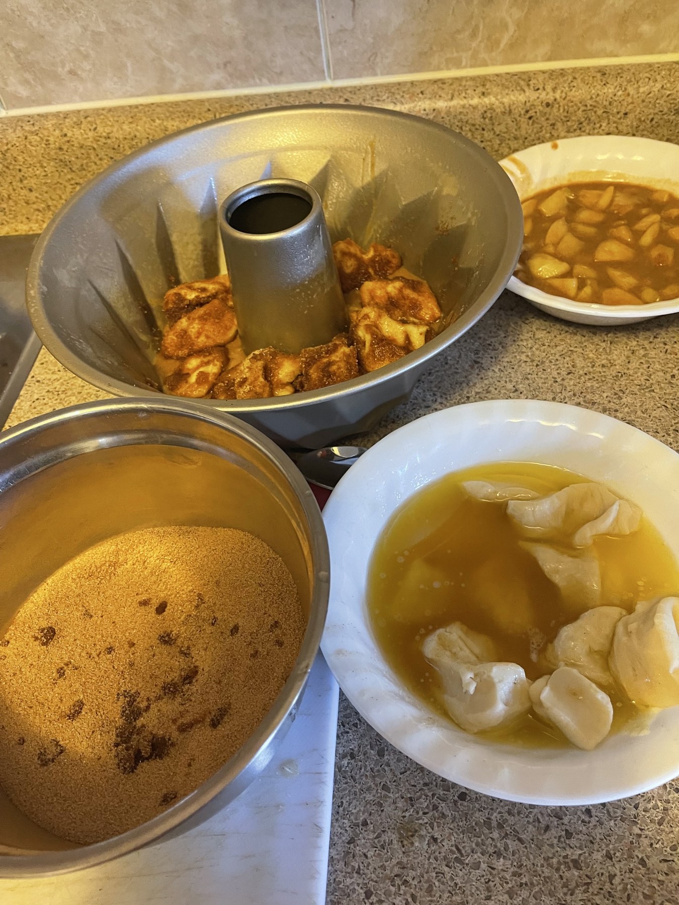 Apple pie monkey bread assembly with dough pieces in melted butter, cinnamon sugar, apple goo, and a Bundt pan