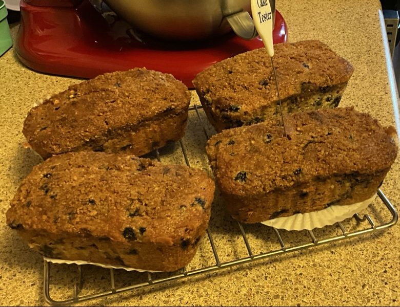 Four mini blueberry loaves cooling on a rack, one with a cake tester
