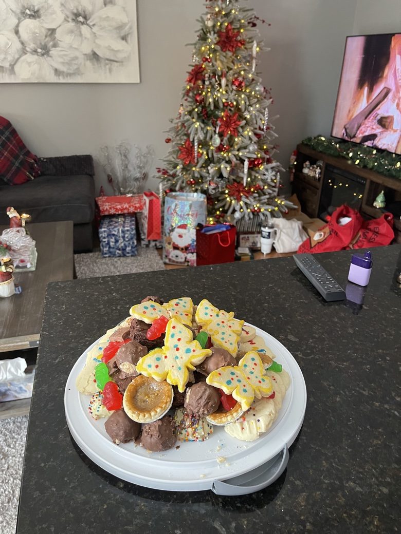 A large plate of Christmas treats and decorated butterfly cookies in front of a Christmas tree