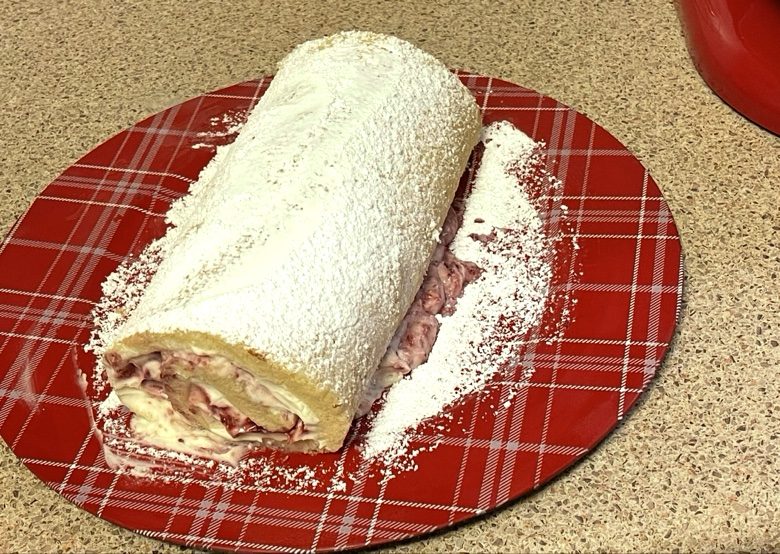 Custard cream roll dusted with powdered sugar on a red plaid plate