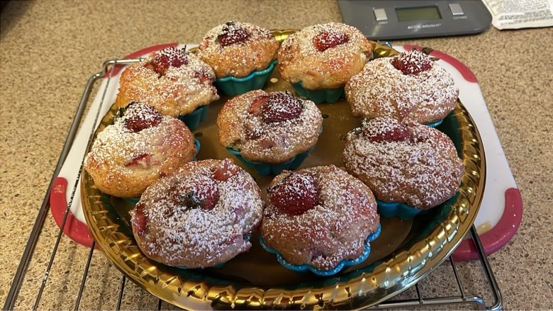 Nine strawberry muffins in teal cups on a gold tray, dusted with powdered sugar